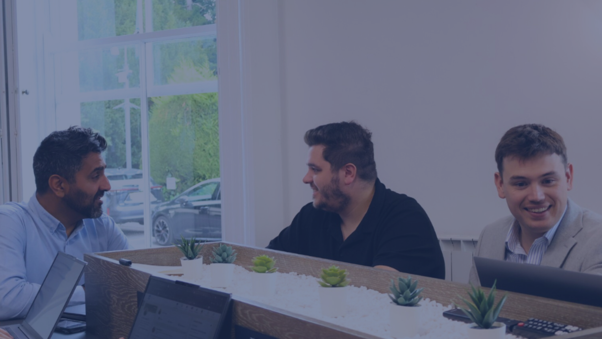 two men sat in front of the window looking at a laptop